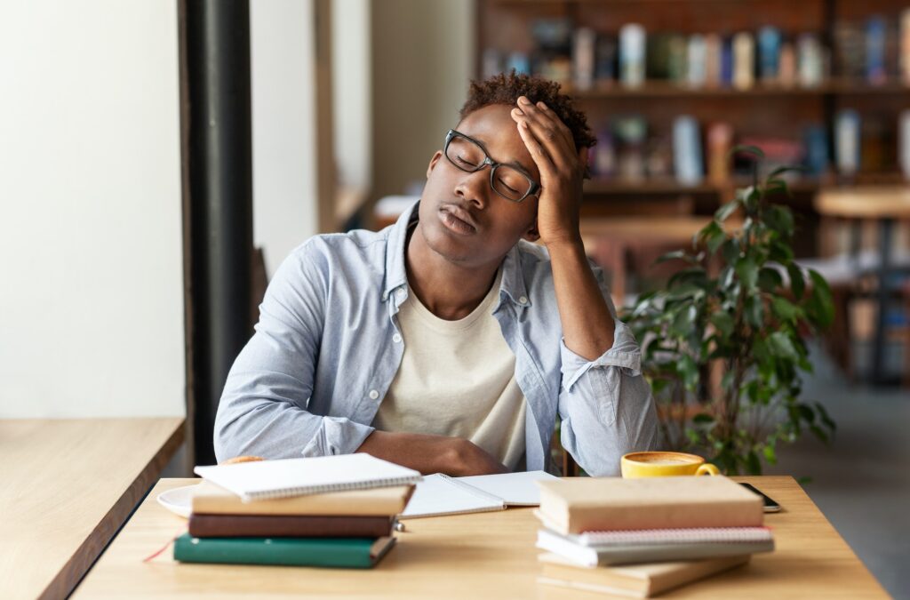 African American guy with books exhausted from studying or working at urban cafe