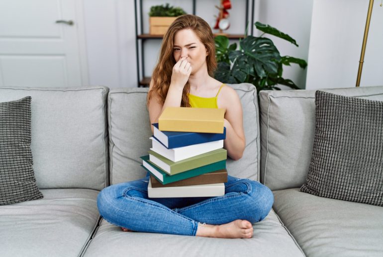 Young,Caucasian,Woman,Sitting,On,The,Sofa,With,Books,At